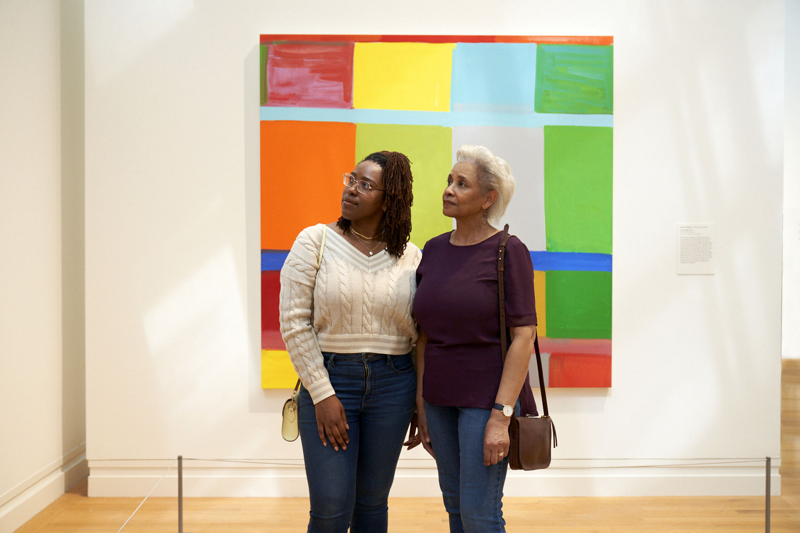 Two Black women, one younger, one older, stand together in knit sweaters and jeans looking at an abstracted, colorful work of art on view in The Met's Modern and Contemporary gallery.